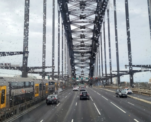Blick durch eine nasse Windschutzscheibe auf die Fahrbahn der Sydney Harbour Bridge